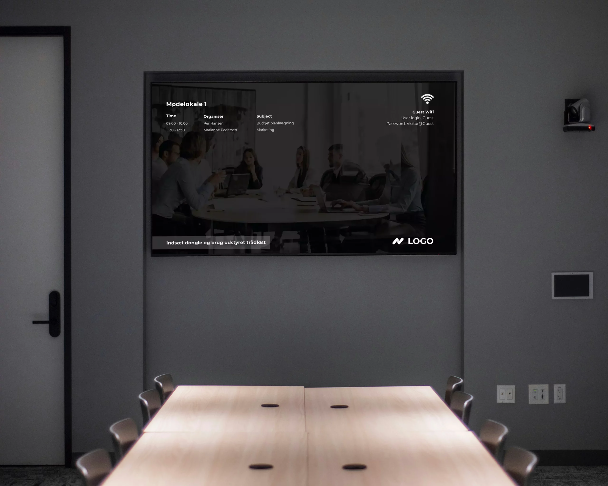 A dark meeting room with a TV on the wall display a screen saver design created using Q-Play Digital Signage.